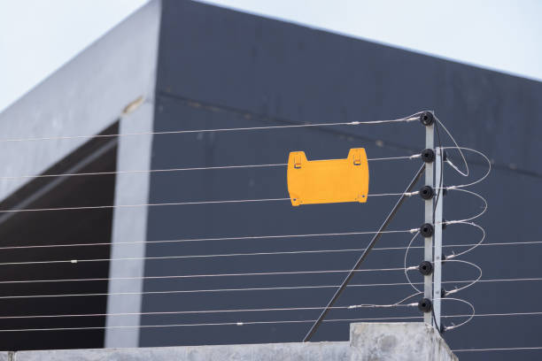 A yellow sign is on a fence next to a building. The fence is made of metal and is attached to a building